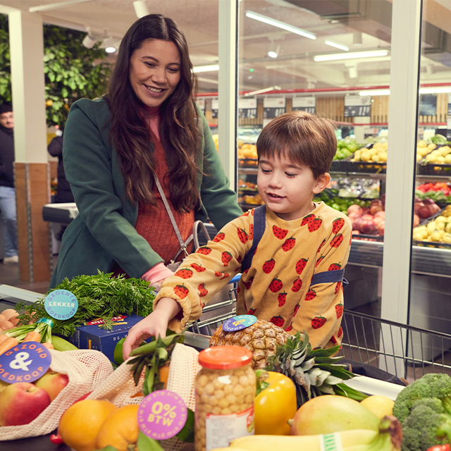 Moeder en kind doen boodschappen op de band bij de kassa. Gezonde producten zoals ananas en paprika